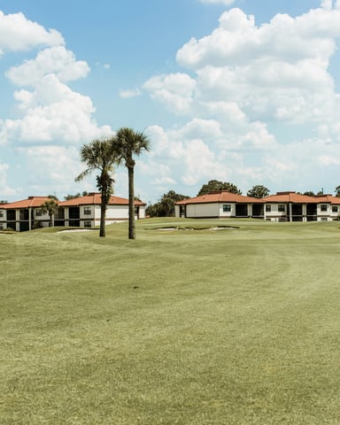 Florida golf course fairway with palm trees, sand bunkers, and resort homes under a blue sky