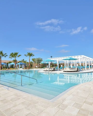 Large resort pool with turquoise water, white pergola, lounge chairs, palm trees, and clear blue sky