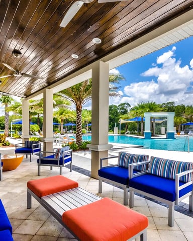 Covered patio with striped lounge chairs and ottomans overlooking resort pool and palm trees