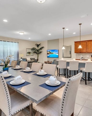 Open-plan dining and kitchen area with large table, upholstered chairs, wood cabinetry, and island seating
