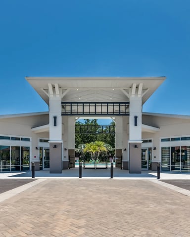 Modern white building with symmetrical design, tall columns, and central breezeway opening to pool area beyond, flanked by landscaping.
