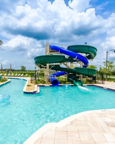 Resort pool with turquoise water, blue and green spiral water slides, palm trees, and loungers under blue sky