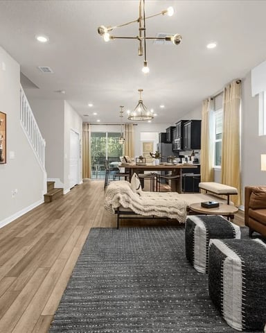 Open-plan living room with brown leather sofa, wood flooring, dark accent wall with TV, and kitchen visible in background