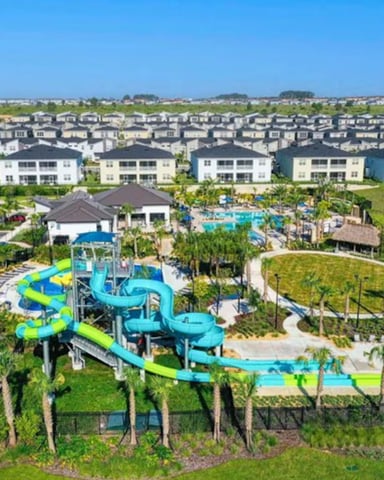 Aerial view of residential community with water park featuring blue and green slides, surrounded by modern homes and green lawns