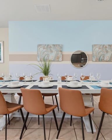 Modern dining room with long white table, orange leather chairs, place settings, and blue accent wall with artwork