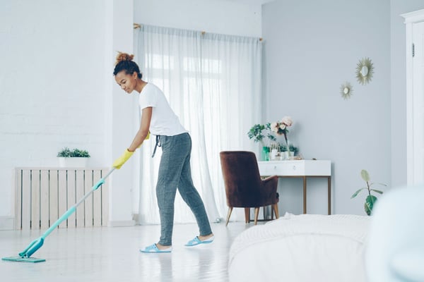 Professional cleaner mopping a bright white bedroom in a vacation rental home